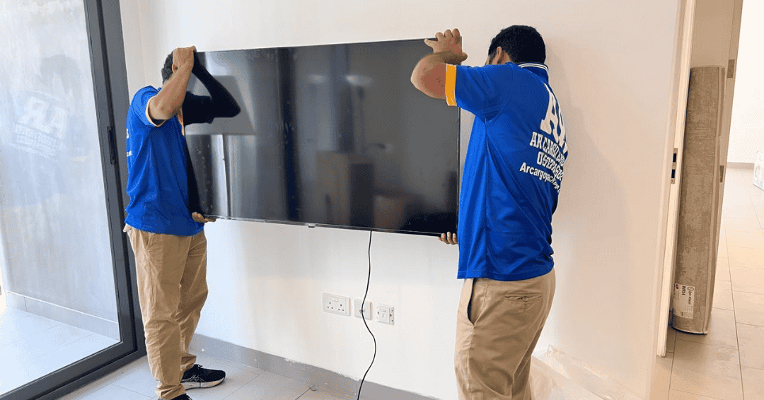 Movers and packers in JVC Dubai safely lifting and setting up a television in an apartment relocation